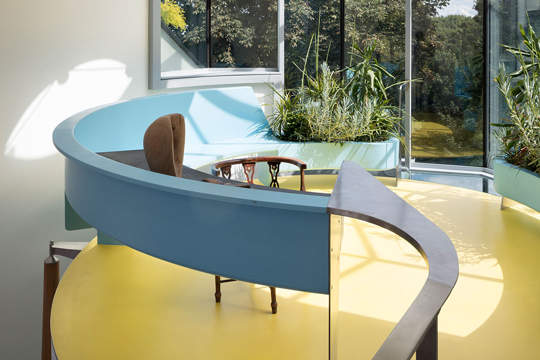 Curved blue desk and yellow floor in the glazed winter garden at 6 Wood Lane, Highgate
